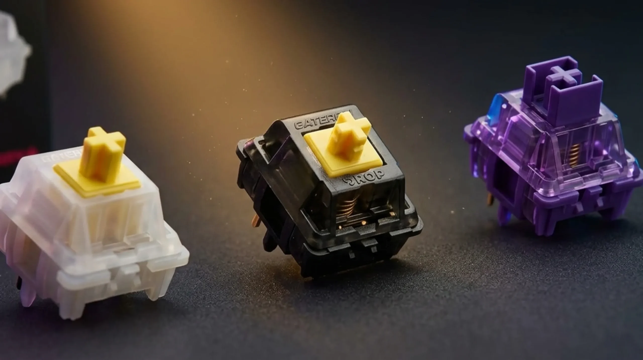 Three mechanical keyboard switches side by side — red linear, brown tactile, and blue clicky — showing internal spring and metal contact leaf in macro detail